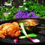 Hel grillad kyckling som ligger på grillgaller bredvid lök och en skål med potatissallad.