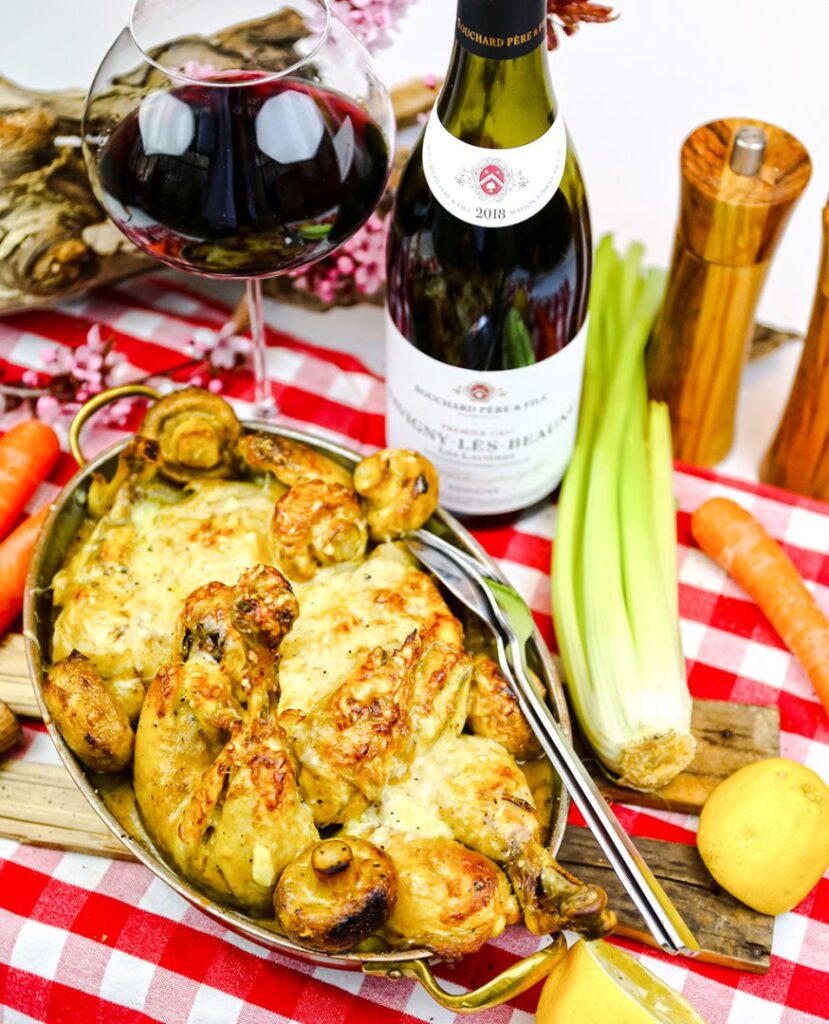 coq a la comtoise på en dukat bord med rutig duk, omringad av primörer och ett glas vin.